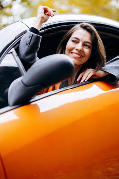 Woman enjoying an autumn drive, smiling and raising her arm from an orange convertible against golden fall foliage