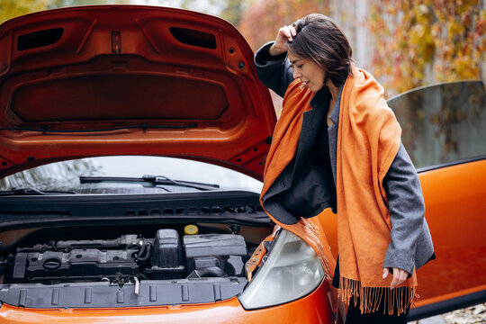 Woman beside open car hood, holding her head and looking down at the engine during a roadside breakdown