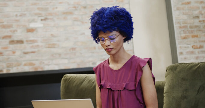 casual businesswoman with blue afro using laptop in office lounge