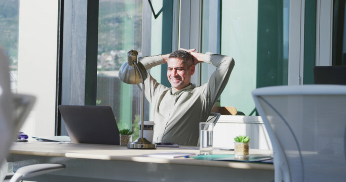 A relaxed businessman uses his laptop at his desk in a casual office setting.