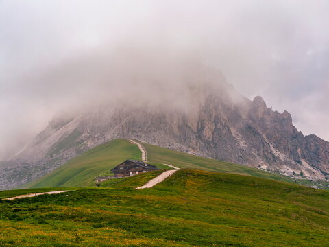 San Vito di Cadore, Italy - 08.07.2016: Isolated wooden alpine hut on green slope under misty grey limestone peaks of the Dolomites