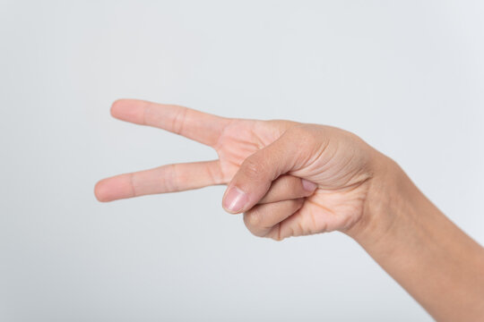Hand showing two fingers in a V sign against a clean white background, symbolizing peace, victory or the number two, close up studio shot of a female hand