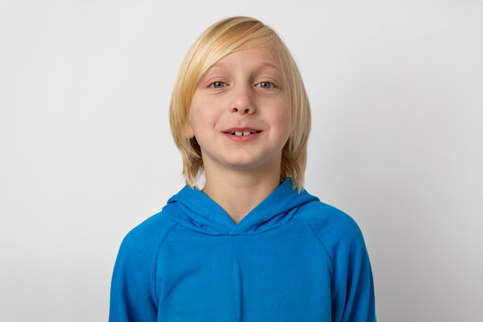 Young blond boy smiling, showcasing a casual and genuine expression, standing against a clean white background, creating an image of childhood happiness and modern innocence