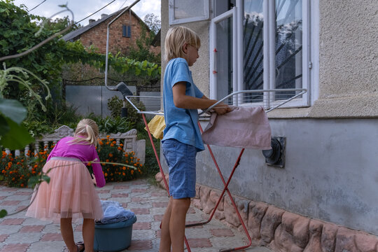 Children are actively participating in household chores, hanging wet laundry on a drying rack in the backyard, showcasing a slice of family life and responsibility