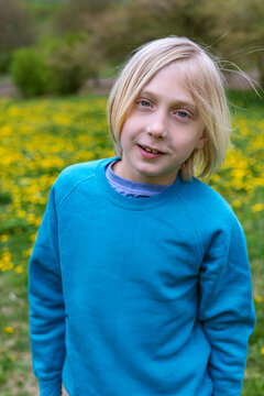 Blond child smiling in turquoise sweatshirt standing in dandelion meadow with soft spring light and shallow depth of field for outdoor portrait use purposes and family lifestyle imagery