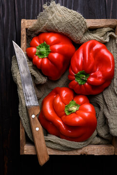 Fresh red bell peppers in rustic wooden crate with kitchen knife. Healthy vegan ingredients, farm produce concept
