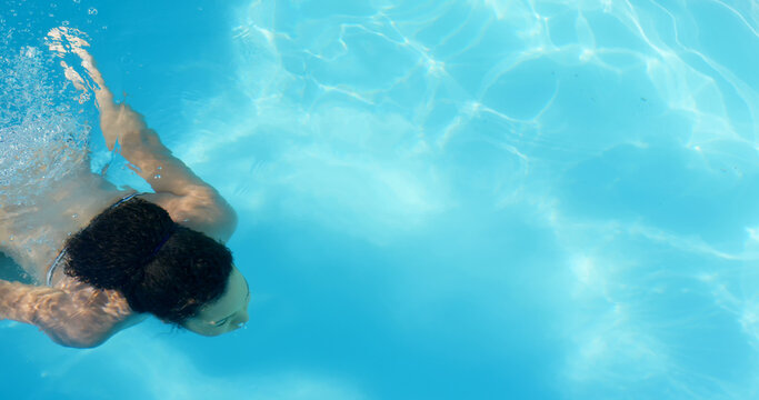 A young woman with dark hair is swimming in clear blue pool