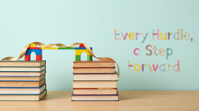 A small toy bridge connects two stacks of books on a wooden desk surface background with hardcover books inspirational inspirational text message bridge spans between message light blue