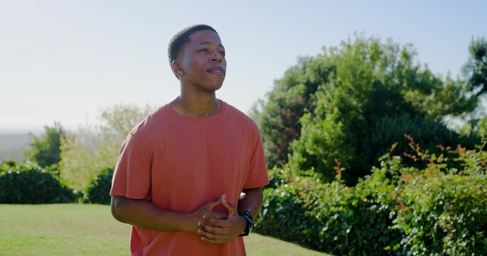 Standing adult man in orange T-shirt clasping hands and gazing upward at backyard lawn, wristwatch