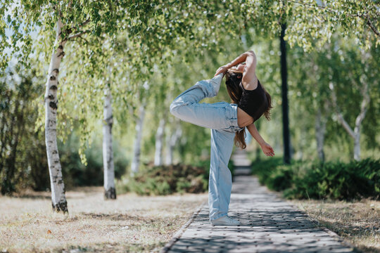 Woman performs a dancer pose while stretching for fitness and flexibility on an outdoor park pathway.