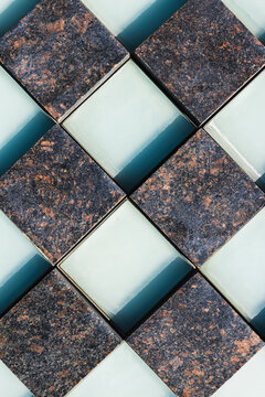 Geometric arrangement of square stone and glass tiles with textured dark surfaces and pale reflective centers in an abstract overhead pattern