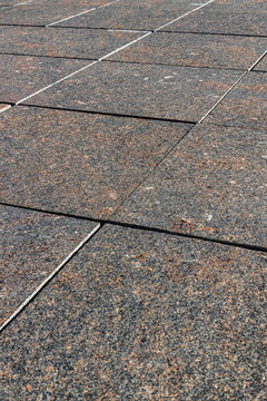 Weathered square paving tiles with speckled gray and brown texture arranged in a geometric pattern across an outdoor paved surface