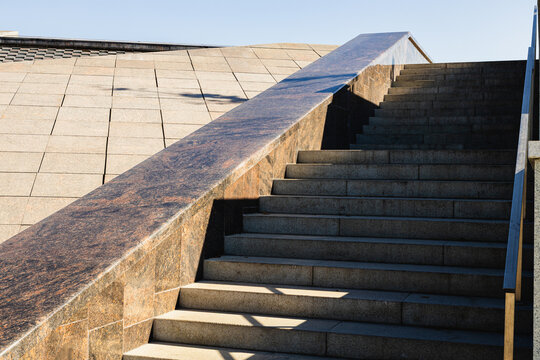 Stone staircase ascending beside a sloped tiled roof with geometric lines and strong sunlight in a modern architectural exterior