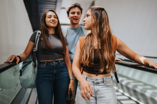 Students and friends ride an escalator together with backpacks inside a university transit building, representing campus commuting and travel.