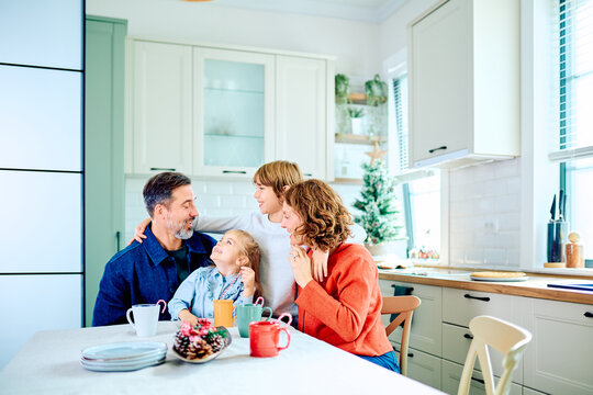 Family gathering around the kitchen table, sharing smiles and holiday warmth during Christmas breakfast beside a decorated tree