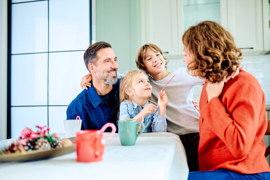 Family sharing a joyful holiday moment around the kitchen table, smiling together over warm drinks and festive treats at home