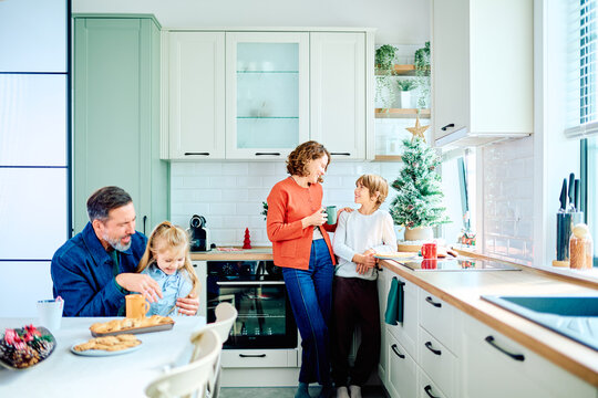 Family sharing cookies and conversation in a bright kitchen, with a small Christmas tree adding a festive holiday touch