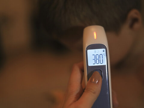 Digital thermometer shows 38&deg;C beside a child's forehead in a temperature check for childhood fever, with a handheld infrared device providing a clear reading for home healthcare and pediatric care.