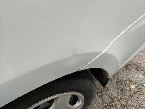Close up of a dented white car body panel with paint damage above a wheel