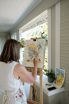 Woman painting watercolor floral still life on an easel in porch