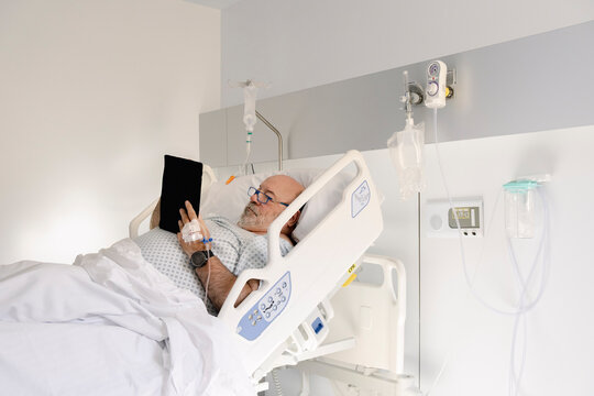 UGC Male patient reading on tablet from hospital bed during recovery