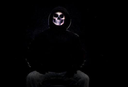 Person wearing a skull mask and black clothes against a black background.