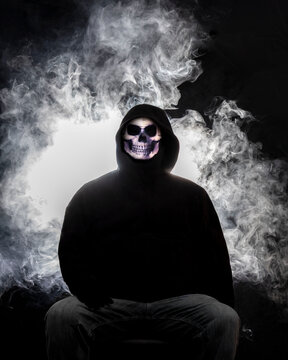 Man wearing a skull mask with smoke in the background.