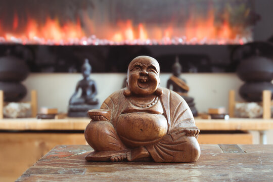 Laughing buddha statue on table with defocused fireplace. Chinese folkloric deity associated with abundance, good luck, contentment and prosperity. Belly rubbing brings good fortune. Selective focus.