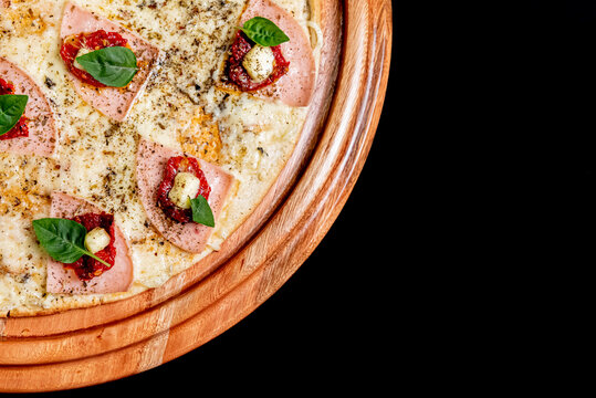 Pizza on wooden board with ham and basil