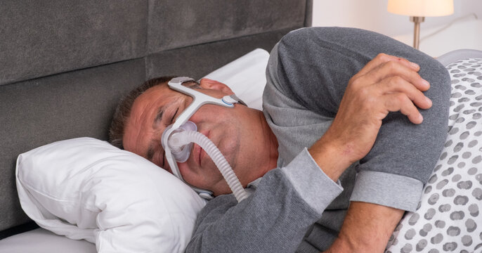 Middle-aged man sleeping on his side wearing a CPAP mask for Sleep Apnea Treatment and prevent breathing pauses during sleep.