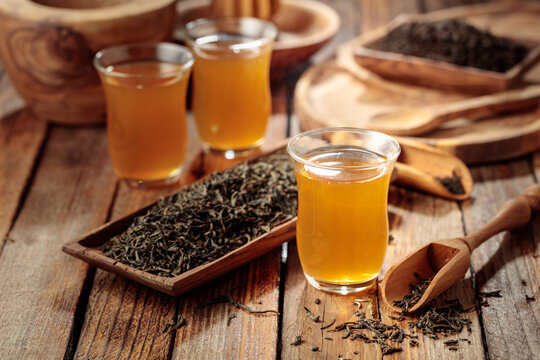 Freshly brewed green tea and dried tea leaves on an old wooden table.
