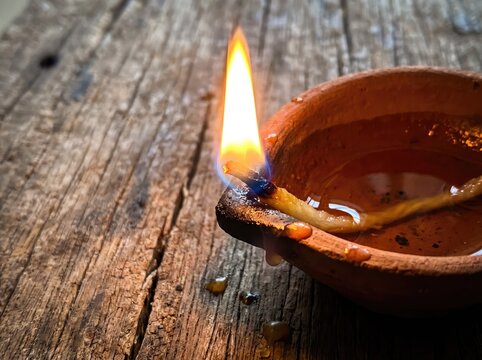 Burning traditional clay diya oil lamp with a bright flame on a rustic wooden surface, symbolizing Diwali, Hindu spirituality, prayer, hope, and light.