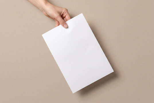 Hand holding blank white sheet of paper on beige background, top view mockup with copy space