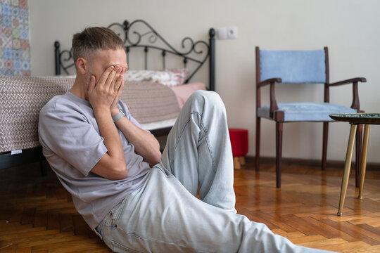 Emotional Breakdown of Adult Man Sitting Alone at Home, Covering Face in Despair and Distress.
