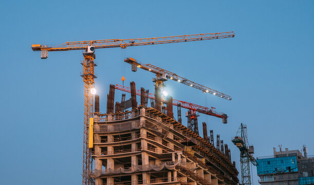 Tower Cranes at Dusk on Concrete Building Construction Site, Urban Development with Evening Lights.