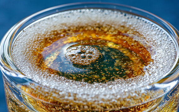 Close up of sparkling wine in glass with many bubbles rising. Golden bubbly champagne liquid fills crystal flute on dark blue background.