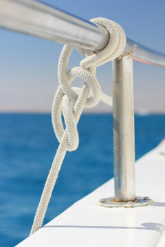 White twisted nautical cord tight knot on stainless steel handrail over blurry sea background closeup