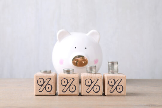 Discount concept. Wooden cubes with percent signs, stacked coins and piggy bank on table