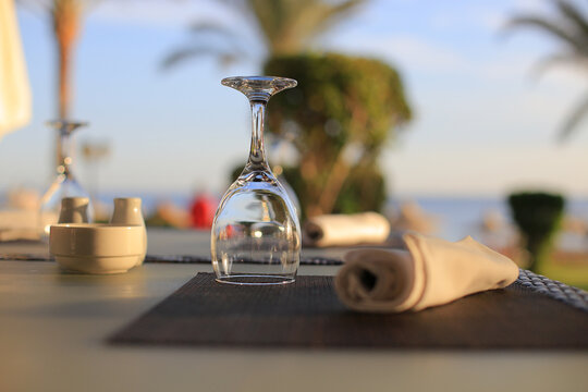 Clean wineglass on dark placemat with rolled textile napkin and tableware on blurry terrace background closeup