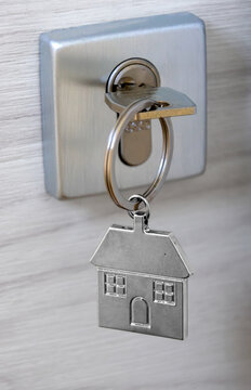 Silver key inserted into a modern door lock, featuring a metallic house-shaped keychain. Concept for real estate, home ownership, buying a new property, moving in, mortgage, and rental investment.
