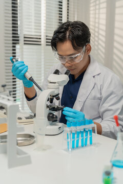 Asian male scientist using micropipette for chemical experiment with microscope in laboratory