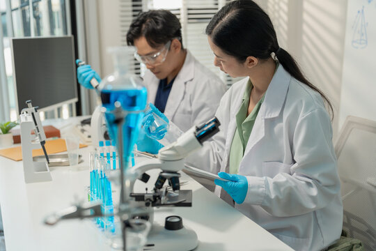 Asian male and female scientists collaborating on research with micropipette and clipboard in laboratory