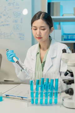 Asian female scientist using dropper with flask and microscope in chemical laboratory