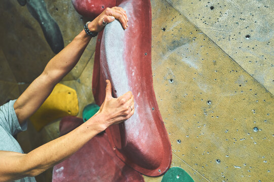 Woman's Hand Gripping a Large Red Climbing Hold on a Bouldering Wall