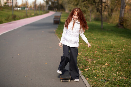 Little Redhead Girl Riding Skateboard In Autumn Park