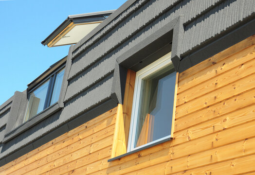 Attic skylight dormer window on modern wooden house with dark tiled roof and timber facade