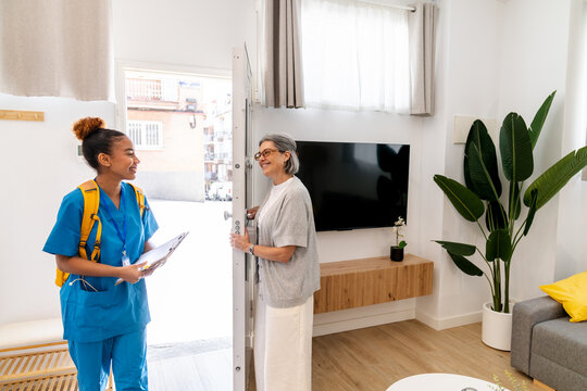 Latina home health nurse greeting an elderly woman at her doorway, building trust during a friendly in home care visit