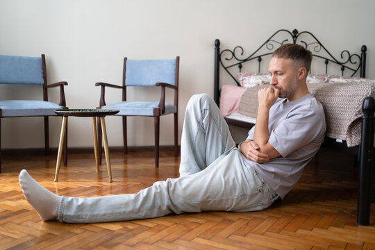Male Loneliness and Social Isolation, Sad Man Sitting Alone on Bedroom Floor Thinking.