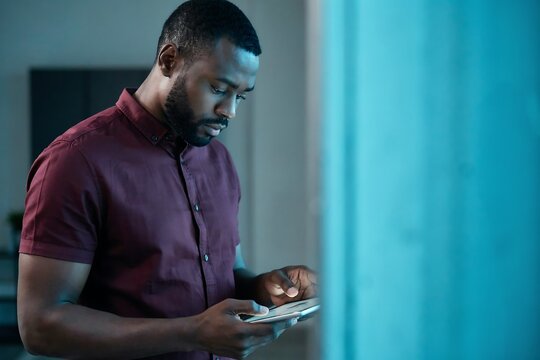 Focused man using smartphone in dark room with blue ambient light for evening work or social media