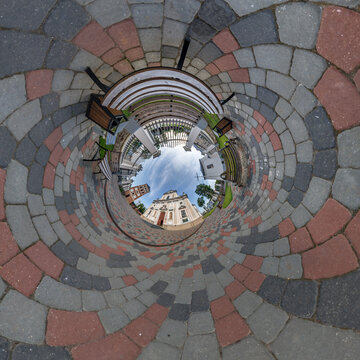 creative tiny planet photo of a rural landscape with dirt road, green fields, and cloudy sky forming a circular world.